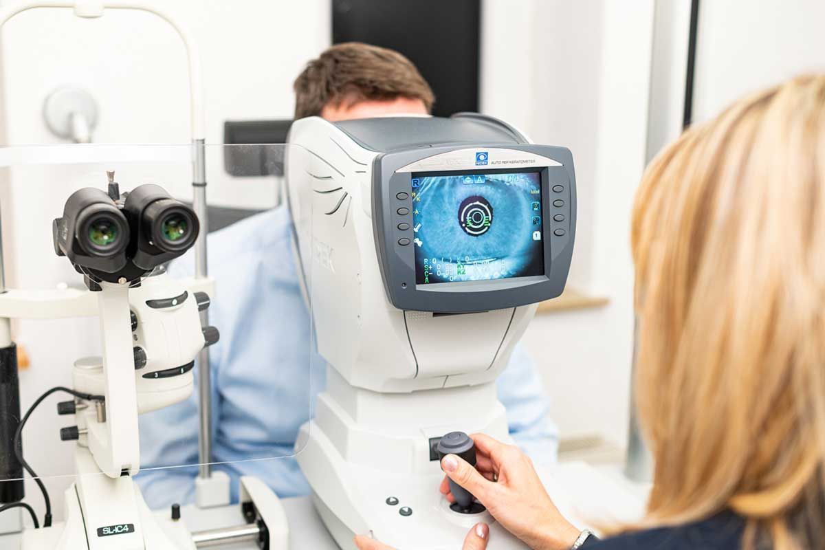 Optiker benutzt ein Augenuntersuchungsgerät an einem sitzenden Patienten in einer hellen Klinik