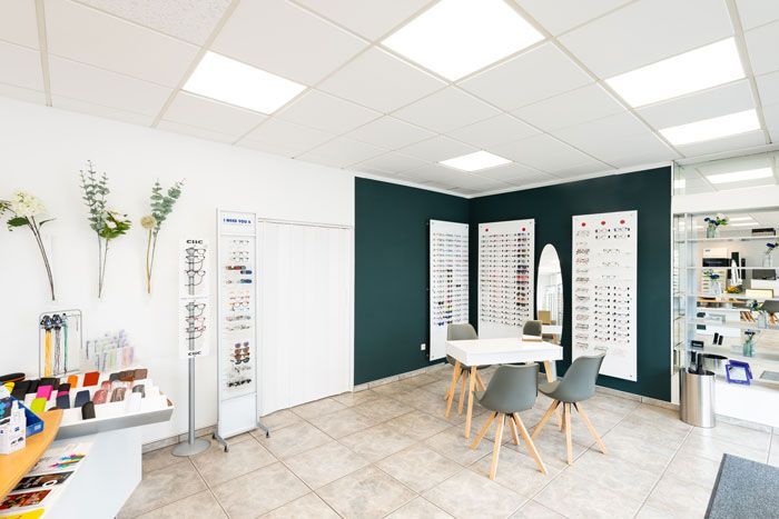 Heller Optiker-Showroom mit Brillenauslagen, weißen Wänden und einem kleinen Beratungstisch
