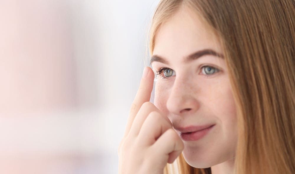 Nahaufnahme einer Frau, die sich in einem hellen, sanft beleuchteten Raum sanft Augen-Make-up aufträgt.