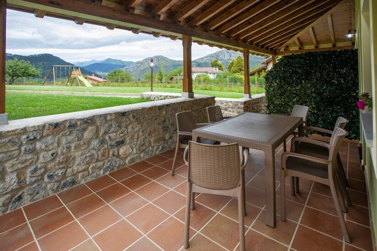 Patio cubierto con sillas y mesa de mimbre, con vistas a un campo verde y a las montañas