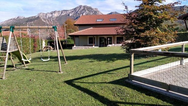 Jardín con césped, columpios, una casa y montañas de fondo bajo un cielo despejado