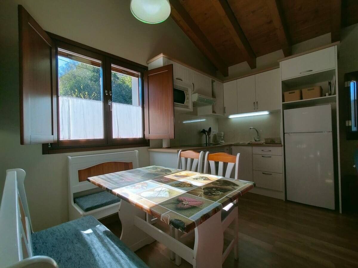Acogedora cocina-comedor con vigas de madera, una ventana abierta y una mesa iluminada por el sol junto a los armarios.