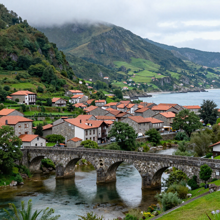Puente de piedra sobre un río en un pueblo con casas de tejados rojos y montañas verdes bajo un cielo nublado