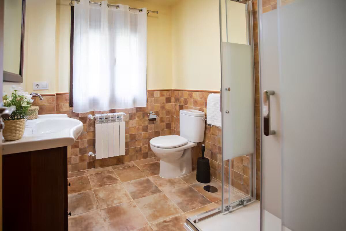 Baño luminoso con lavabo, inodoro, ducha y suelo de baldosas en tonos beige