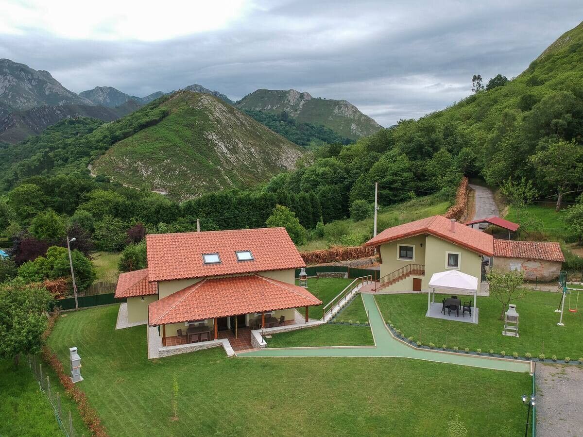 Casas rurales en la ladera, con tejados de tejas rojas, jardines verdes y montañas bajo un cielo nublado