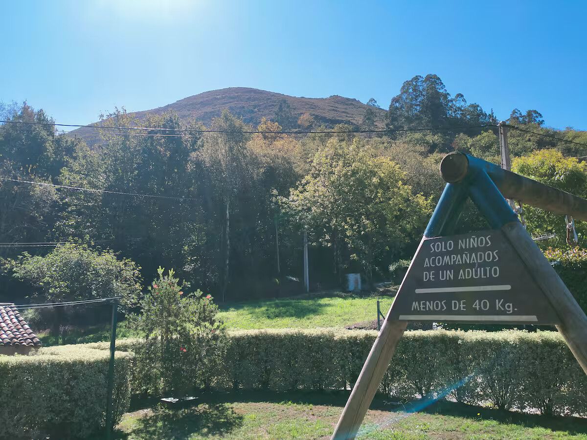 Parque de montaña con un laberinto de setos, una pradera y una señal triangular en primer plano bajo un cielo azul