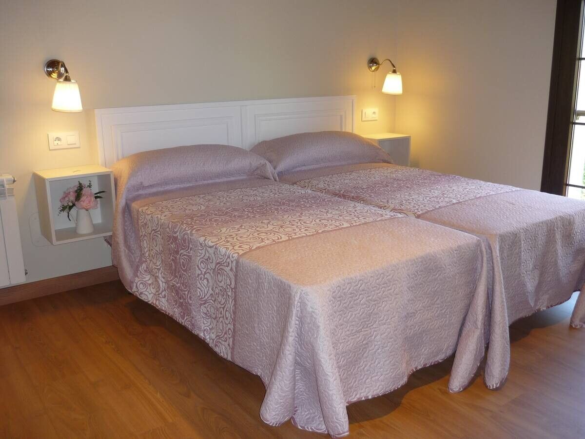 Dos camas individuales en un dormitorio con luz tenue, suelo de madera y lámparas de mesita de noche