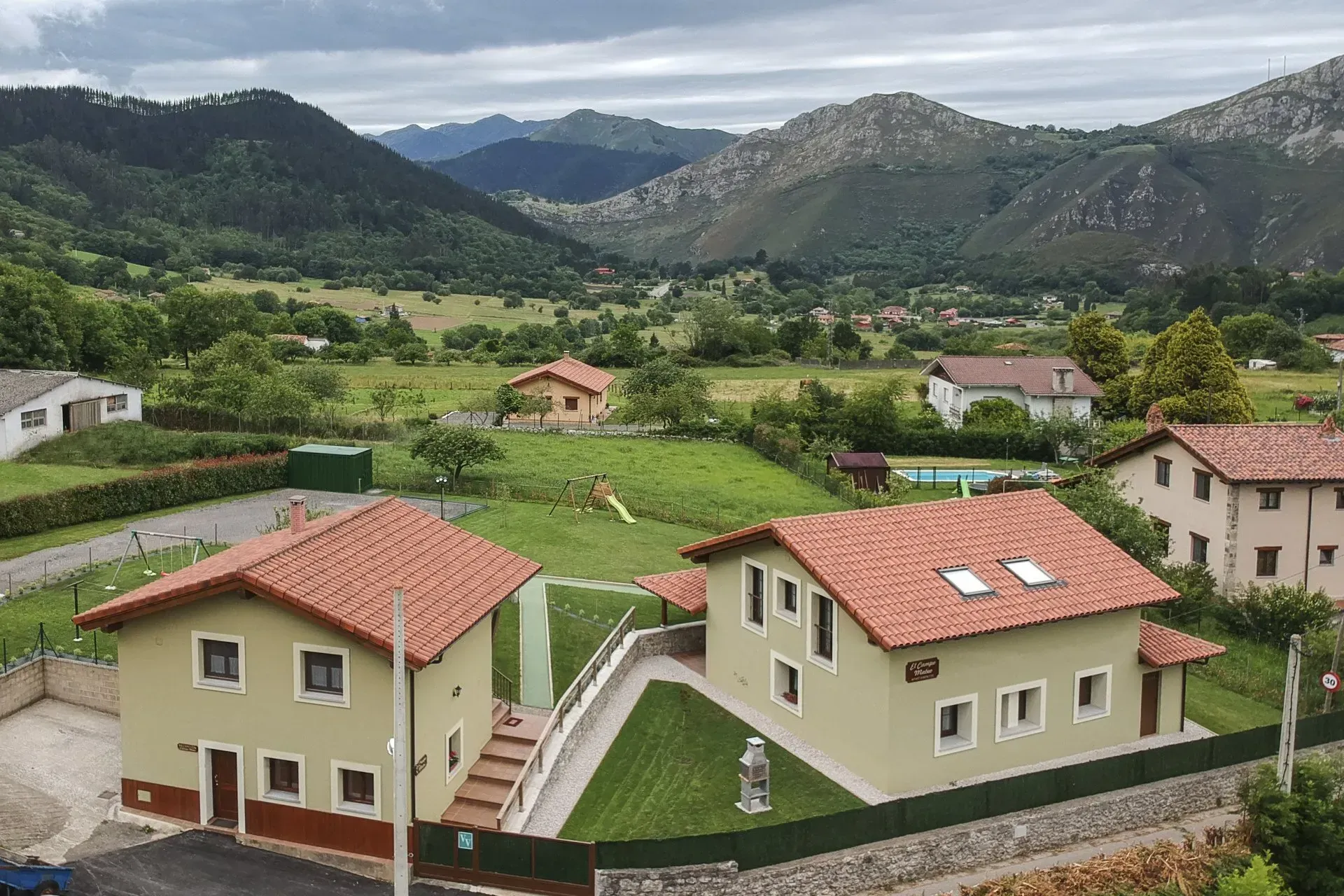 Casas rurales en la ladera, con tejados rojos, que dominan campos verdes y montañas bajo un cielo nublado
