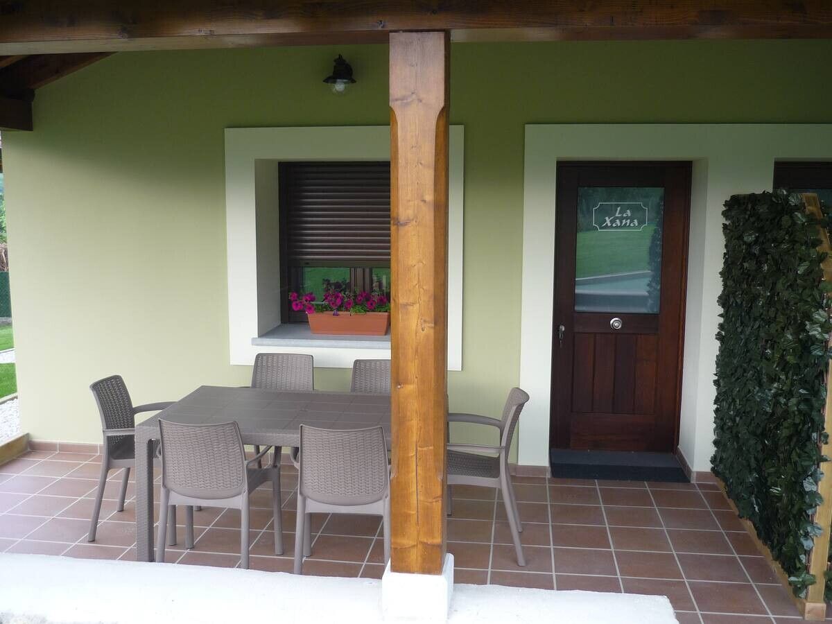 Patio cubierto con mesa y sillas de comedor junto a una puerta principal de madera y una ventana, enmarcado por paredes verdes y azulejos