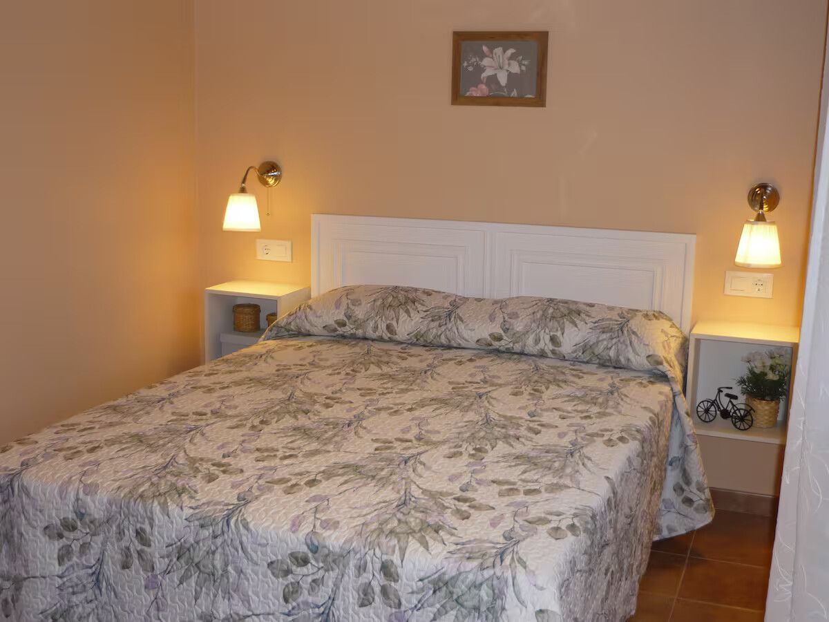 Dormitorio con colcha de flores, cabecero blanco, lámparas de mesilla y un cuadrito en la pared