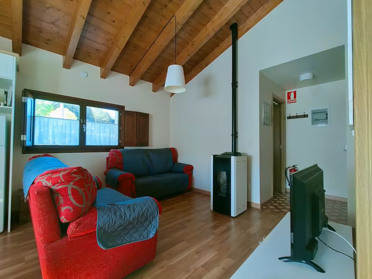 Acogedora sala de estar con un sillón rojo, un sofá azul, techo de madera, estufa y televisor junto a la pared.