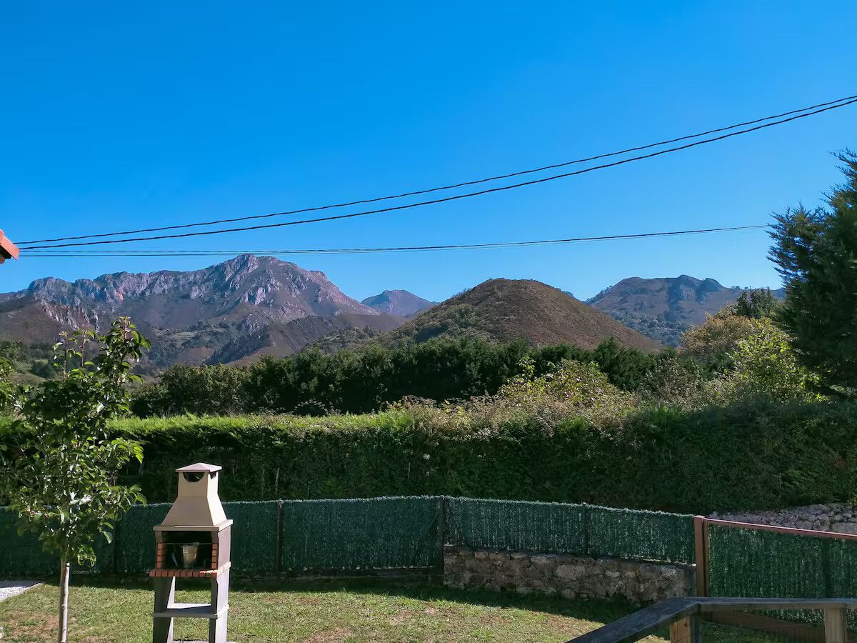 Patio trasero con barbacoa, setos verdes y montañas bajo un cielo azul despejado