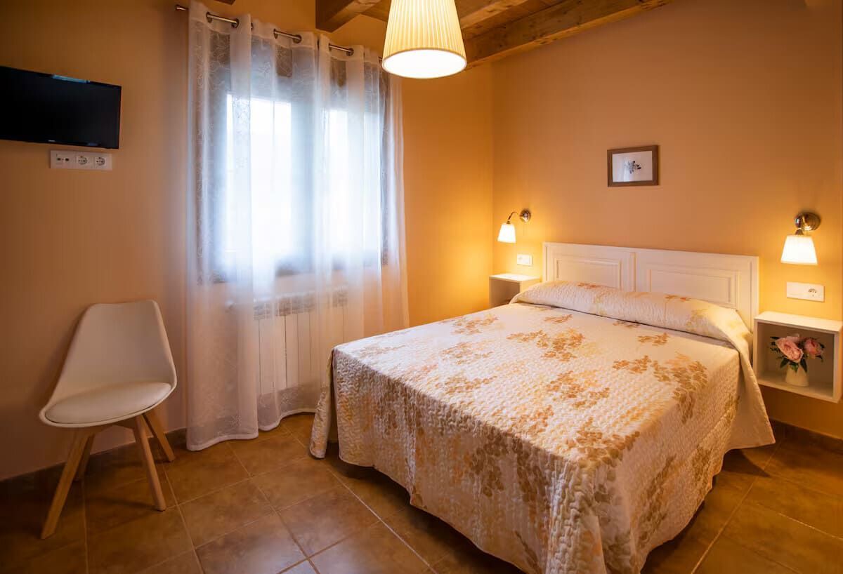 Dormitorio acogedor con cama doble, paredes de un cálido tono naranja, cortinas blancas y una silla junto a la ventana