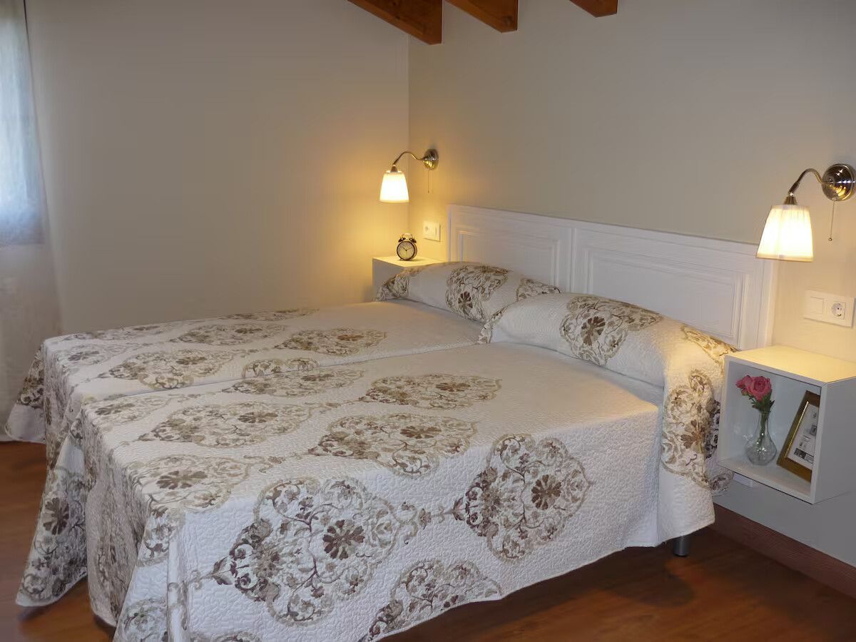 Dormitorio con una cama cubierta con una colcha floral beige, iluminado por apliques de pared y lámparas de mesilla