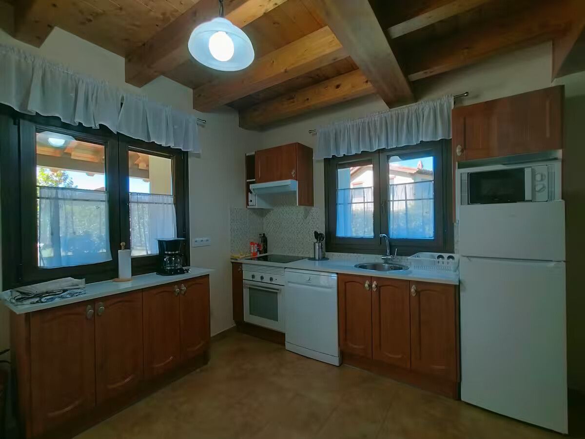 Cocina compacta con armarios de madera, electrodomésticos blancos y vigas de madera a la vista en el techo.