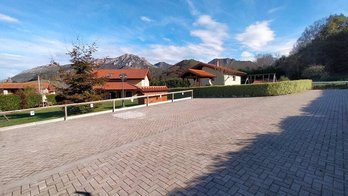 Amplio patio pavimentado con ladrillos junto a casas, árboles y setos, bajo un cielo azul despejado