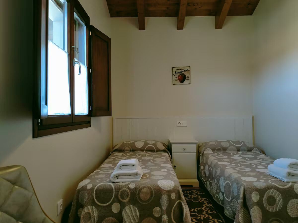 Dormitorio pequeño con dos camas individuales, una ventana y vigas de madera a la vista en el techo.