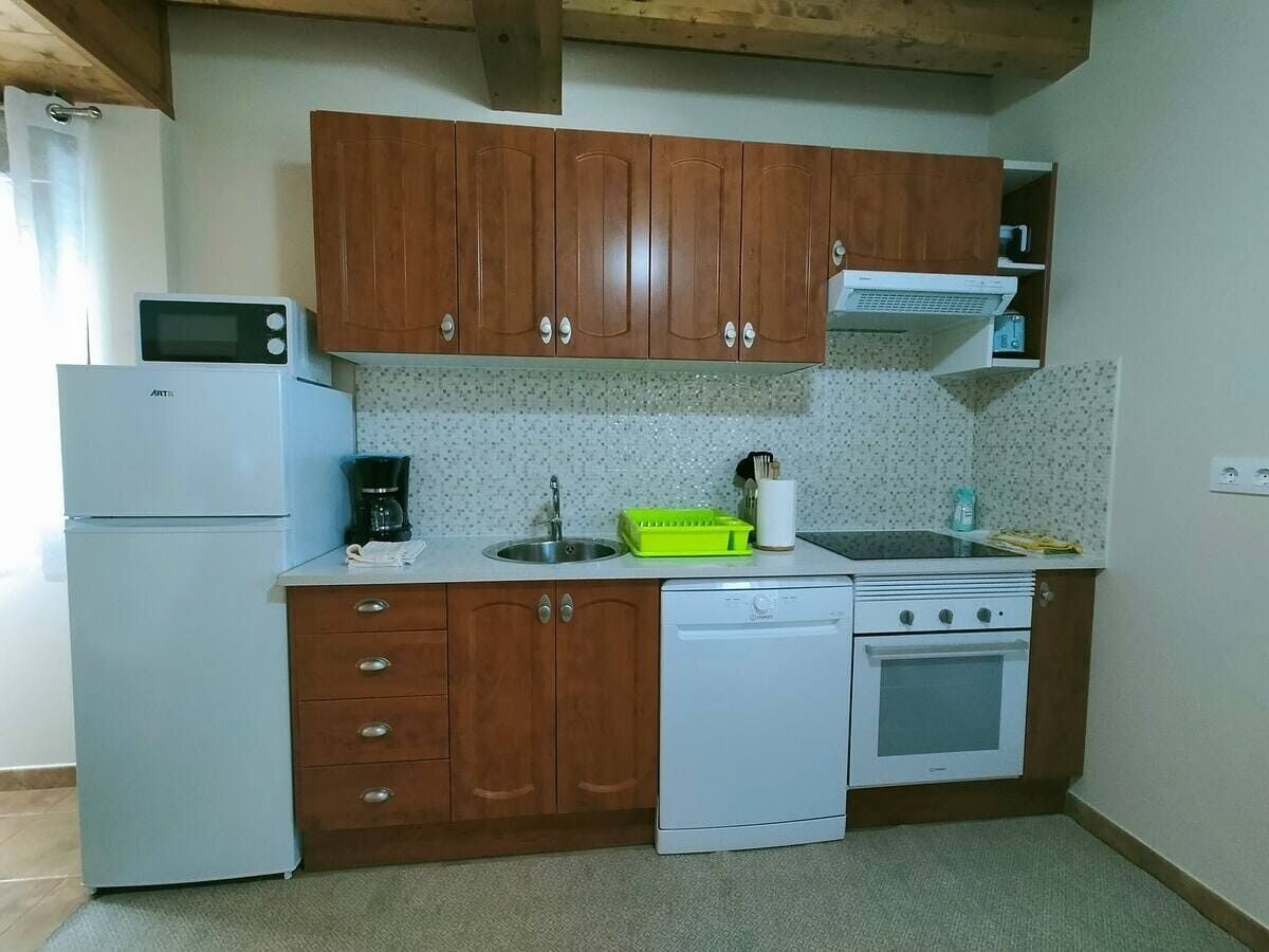 Cocina compacta con electrodomésticos blancos, armarios de madera y un microondas encima del refrigerador