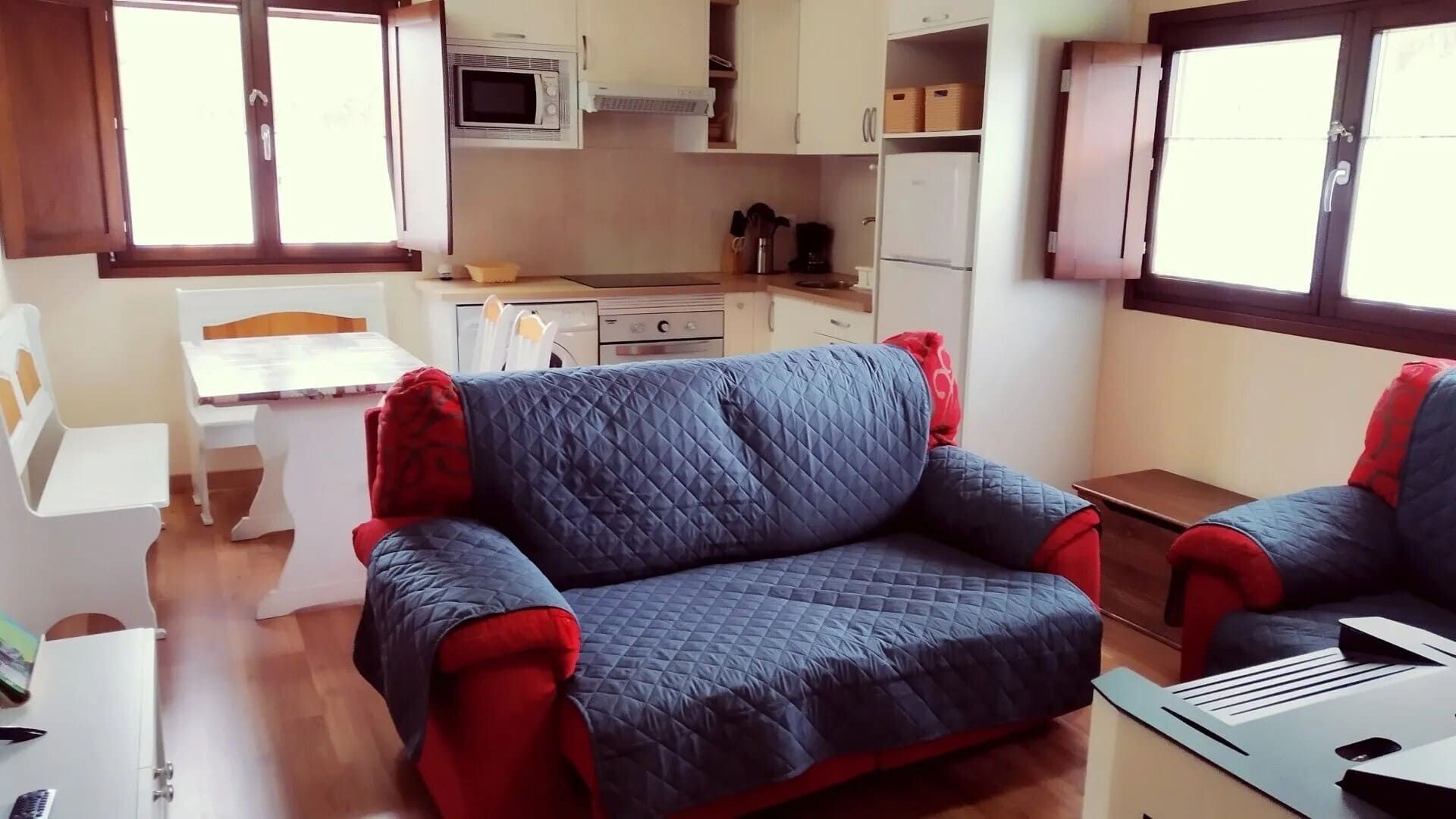 Acogedor salón con sofás azul y rojo, comedor blanco y una cocina al fondo