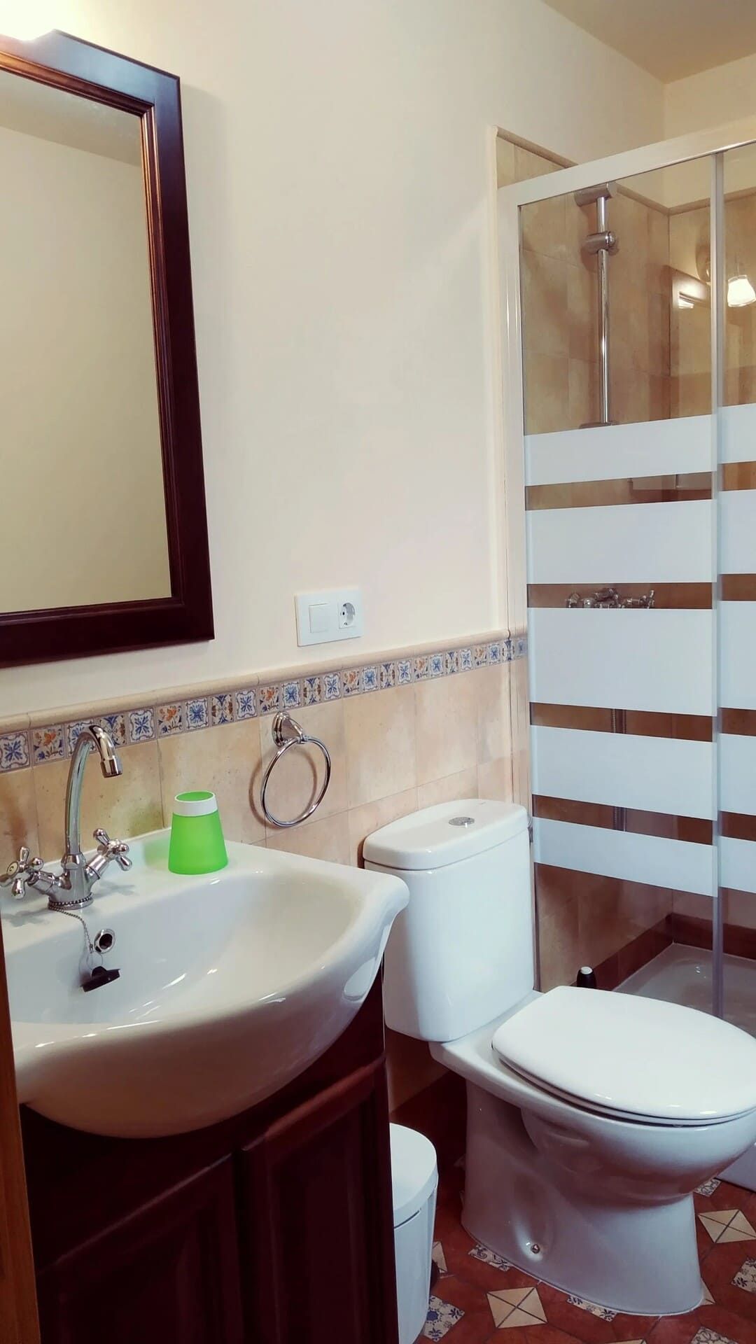 Baño con lavabo, espejo, inodoro y mampara de ducha de cristal con puertas a rayas marrones.