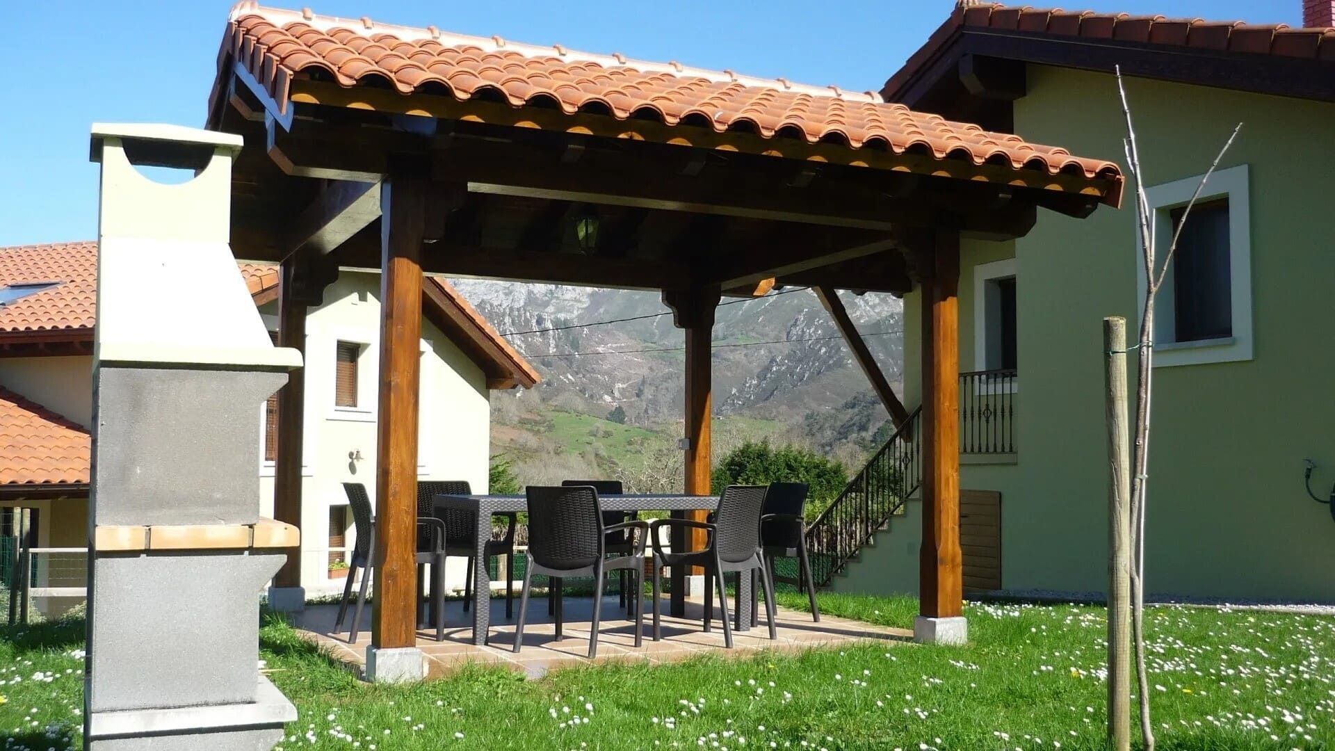 Patio exterior con techo de tejas, mesa y sillas, parrilla y vistas a las montañas de fondo