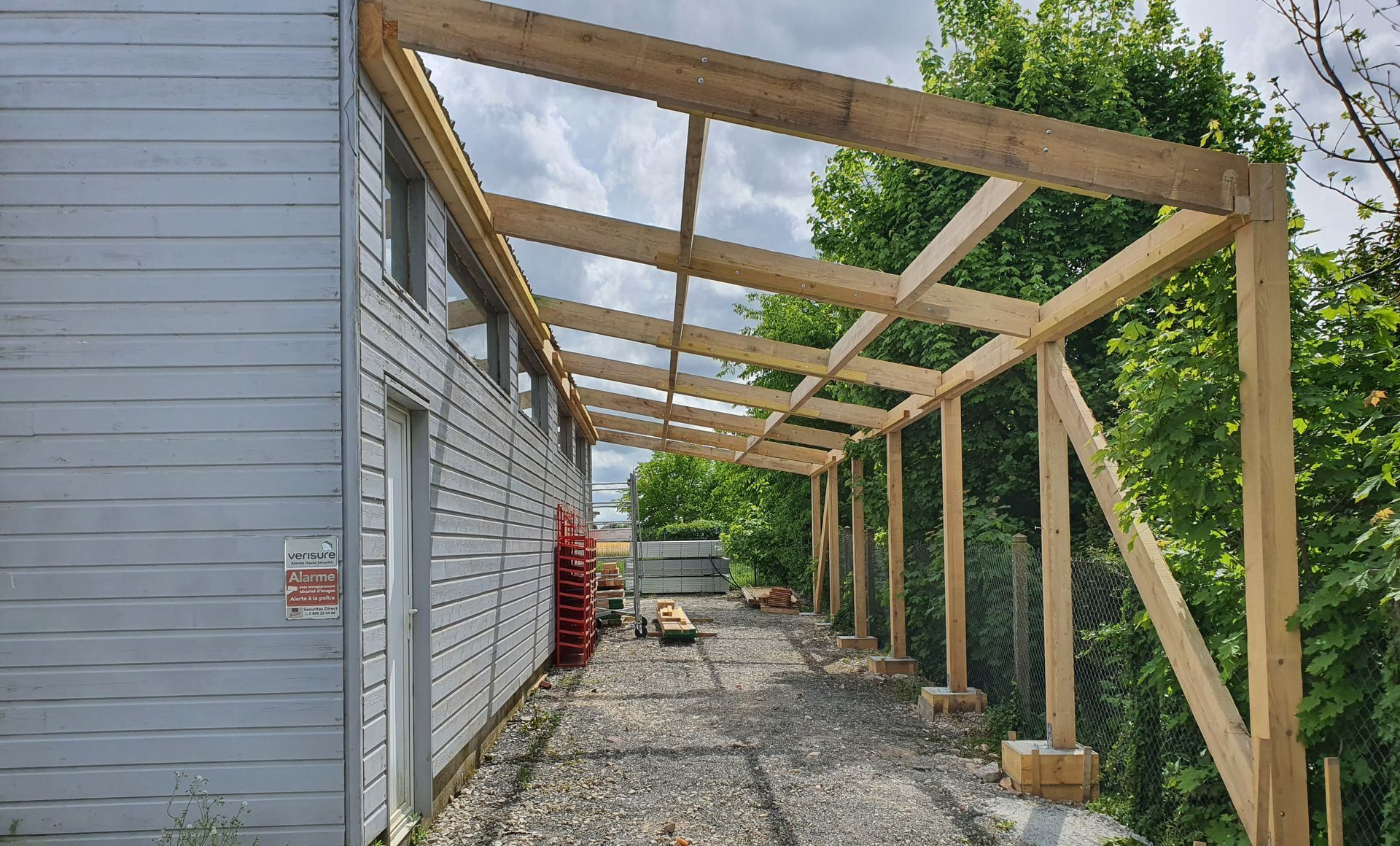 Charpente de carport adossée à un mur gris