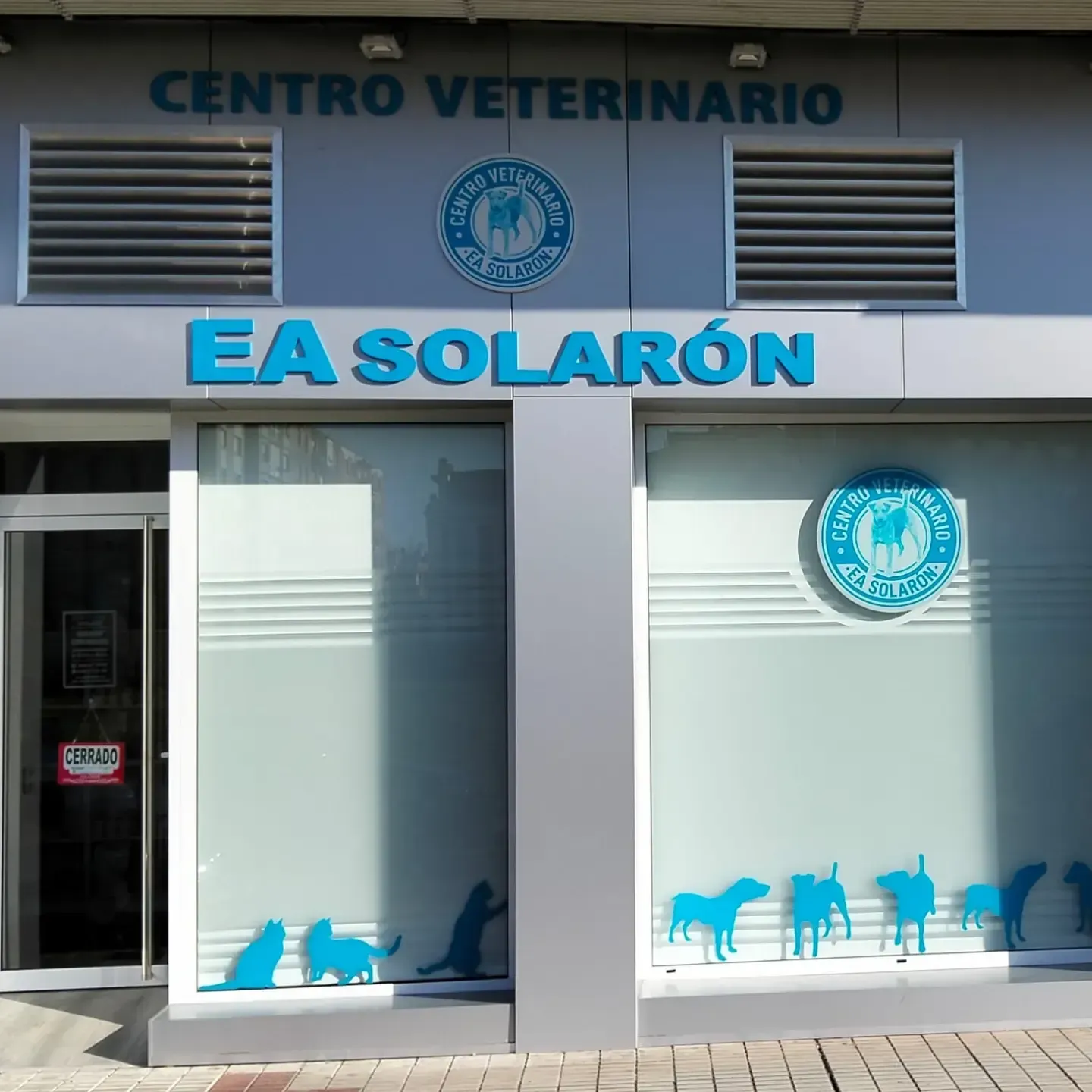 Exterior del Centro Veterinario EA Solarón con letreros azules y siluetas de mascotas en las ventanas.