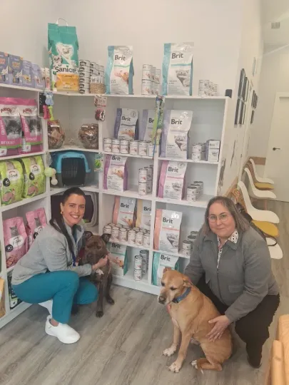 Dos personas se arrodillan con un perro en un pasillo de una tienda de mascotas, junto a estantes llenos de productos para animales.