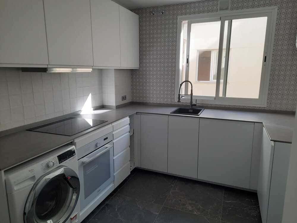 Una cocina con gabinetes blancos, lavadora y secadora, un fregadero y una ventana.