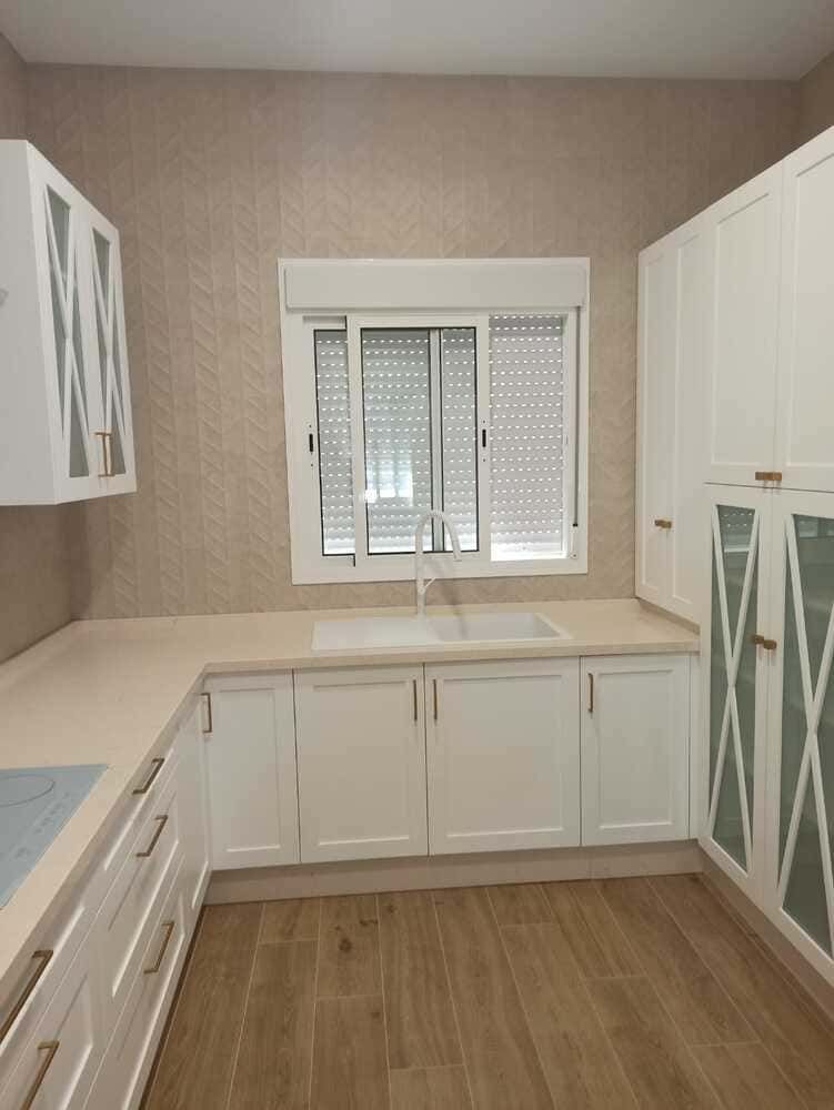 Una cocina con gabinetes blancos, un fregadero y una ventana.