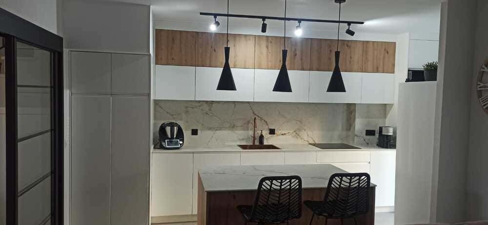 Una cocina con gabinetes blancos, gabinetes de madera, un fregadero y dos sillas.