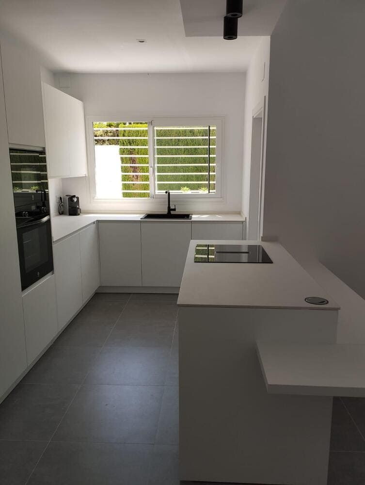 Una cocina con gabinetes blancos, un horno, un fregadero y una ventana.