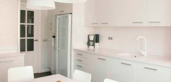 Una cocina con gabinetes blancos, un refrigerador, un fregadero y una mesa.