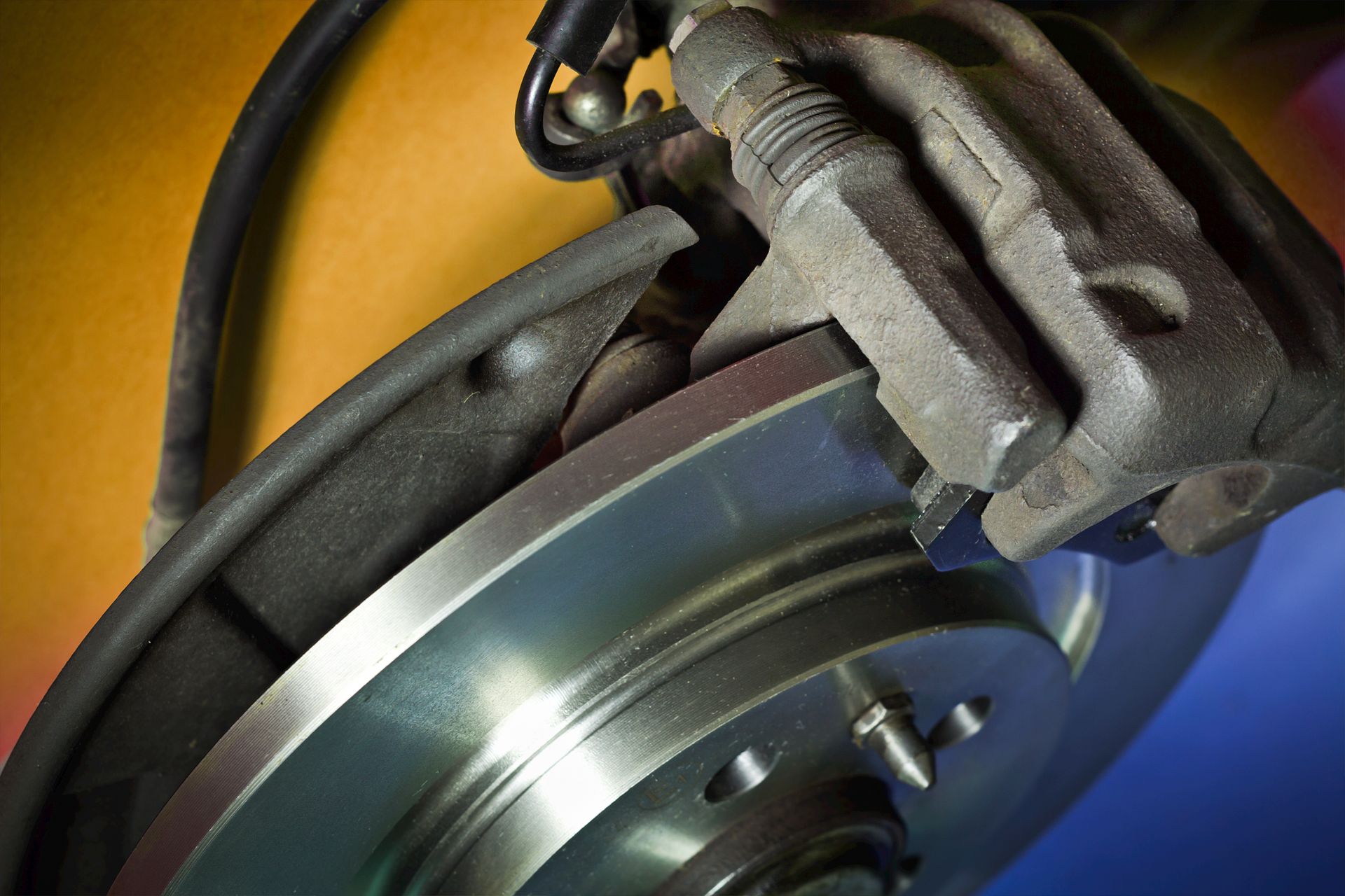 Gros plan sur un disque et un étrier de frein de voiture ; argent et noir sur fond coloré.