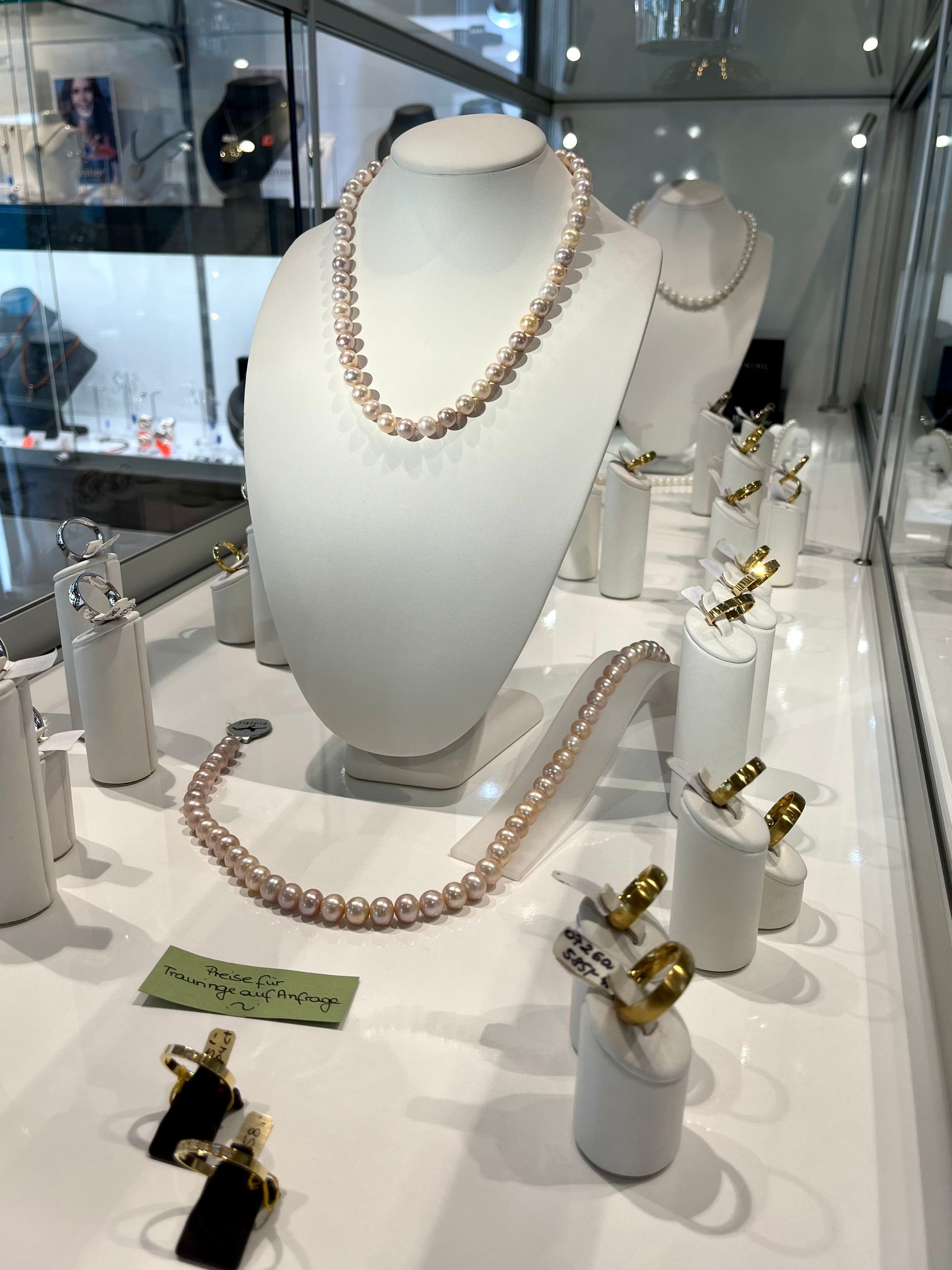 Schmuckvitrine mit Halsketten, Armbändern und Ringen; rosa Perlen.