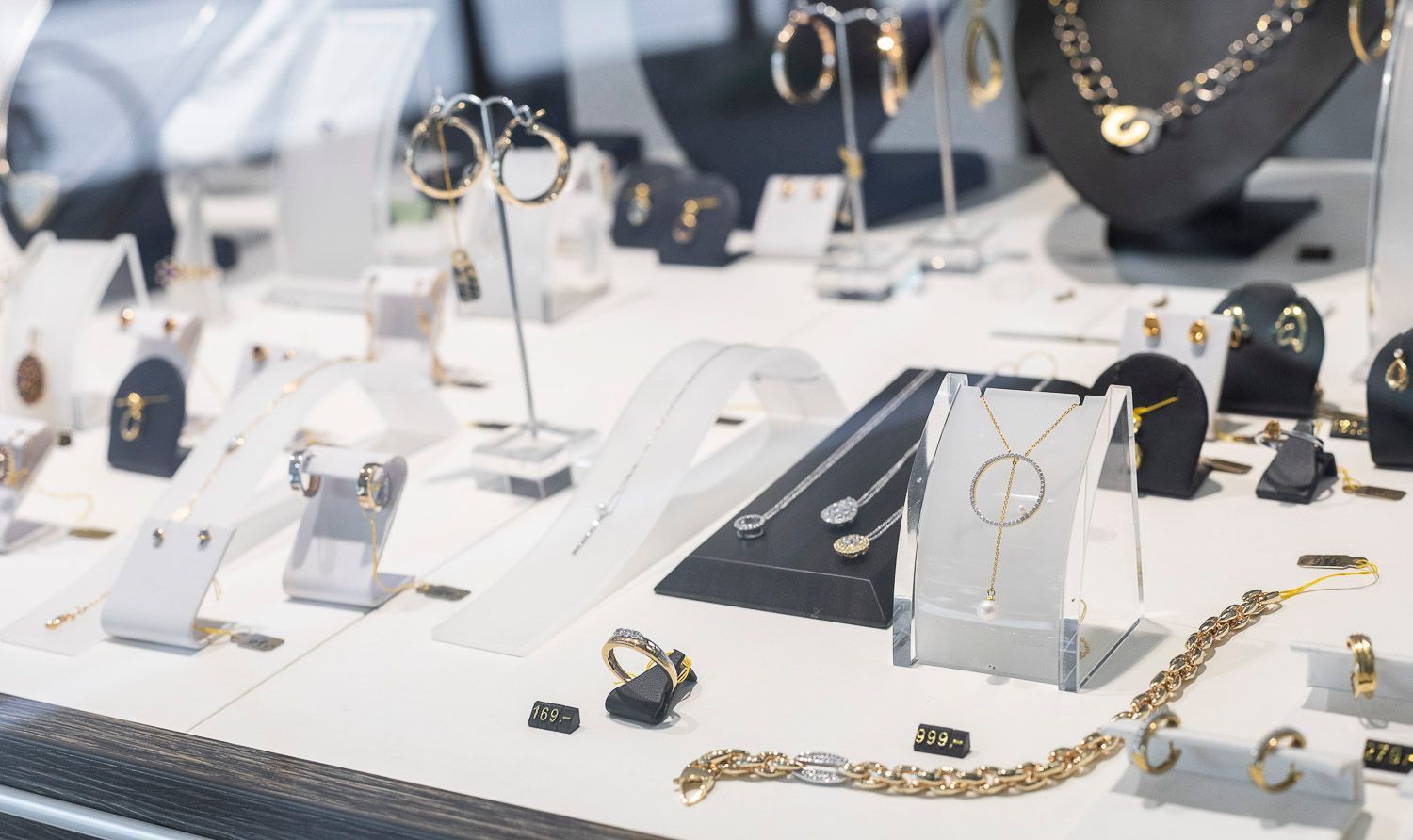 Schmuckausstellung in einem Geschäft mit goldenen Halsketten, Ohrringen und Ringen auf weißen und schwarzen Ständern.