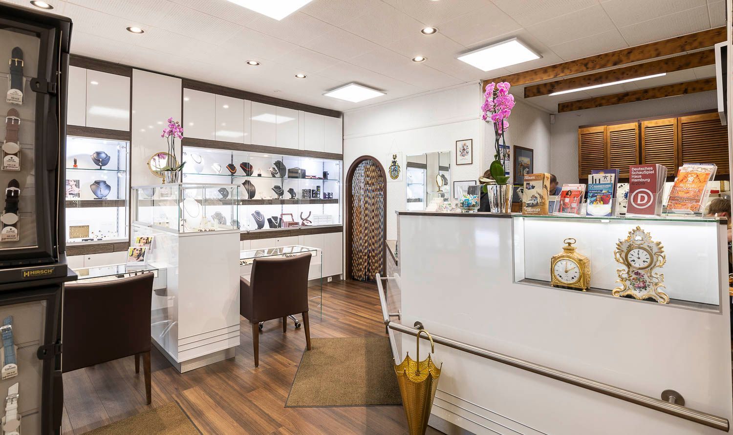 Innenraum eines Juweliergeschäfts mit Uhren und Schmuck in Vitrinen, weiß-braunes Dekor.