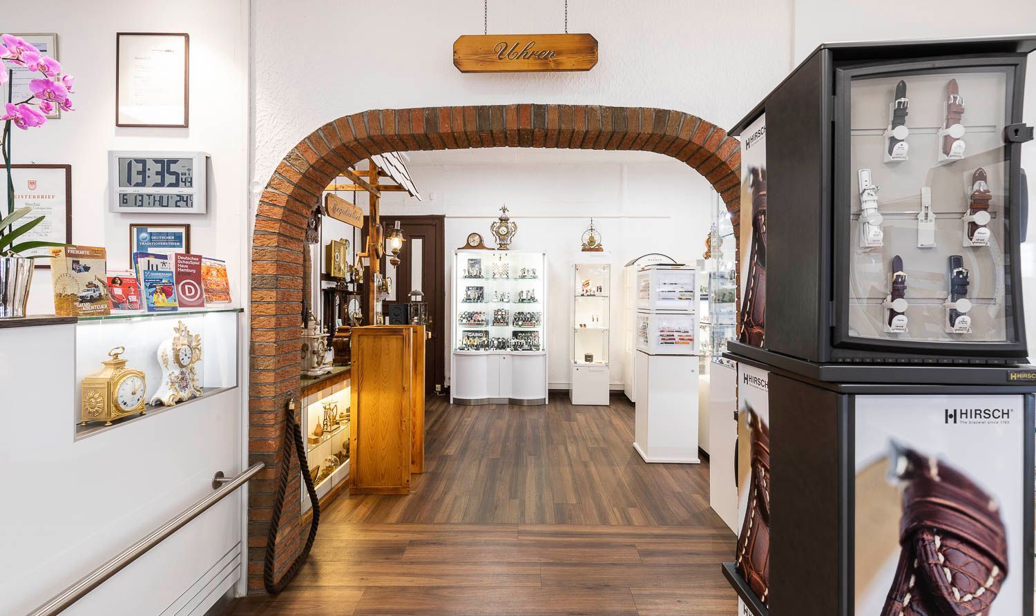 Innenansicht eines Juweliergeschäfts mit gewölbtem Ziegeleingang, ausgestellten Artikeln und Uhren in einer Glasvitrine.