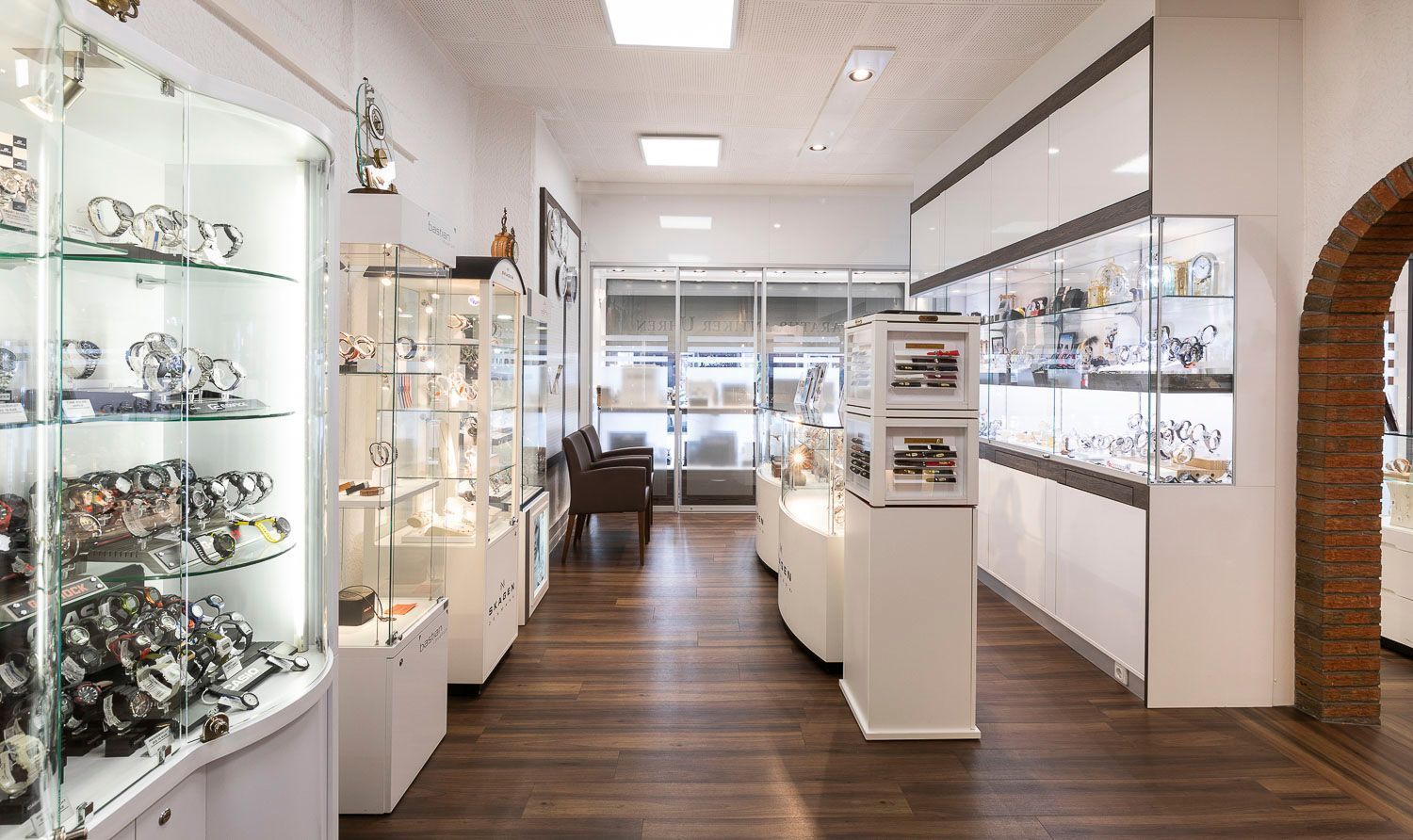 Inneneinrichtung eines Juweliergeschäfts mit Vitrinen, in denen Uhren und Schmuck auf Holzböden präsentiert werden.