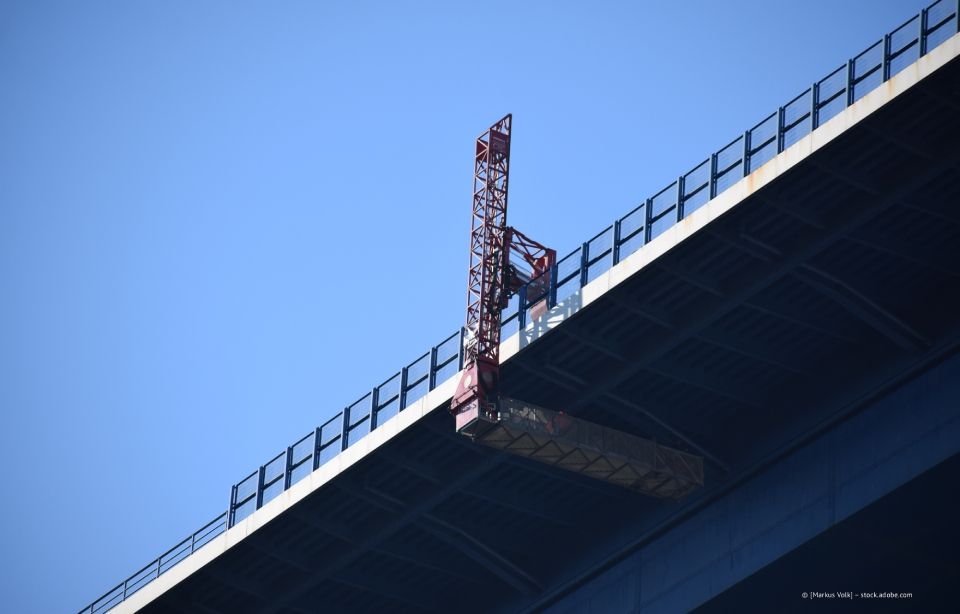 Ein Bauarbeiter reinigt auf einer Plattform die Fenster eines hohen Glasgebäudes.