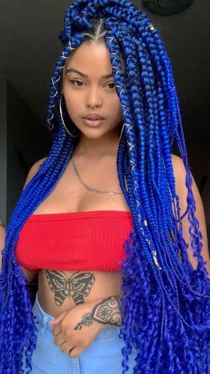 Mujer con largas trenzas azules, vistiendo un top rojo tipo tubo, mirando hacia la cámara.