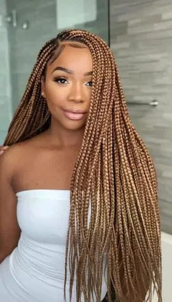 Mujer con largas trenzas rubias, vestida con un top blanco sin tirantes, en un baño.