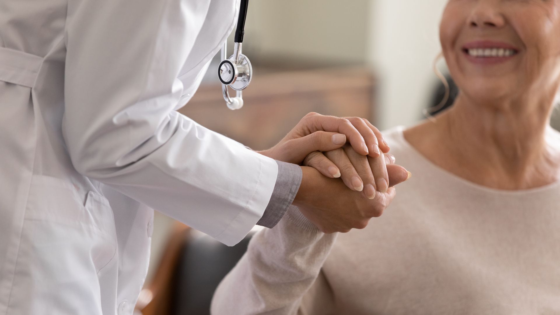 Eine medizinische Fachkraft schüttelt in einem hellen Klinikzimmer einem lächelnden Patienten die Hand.