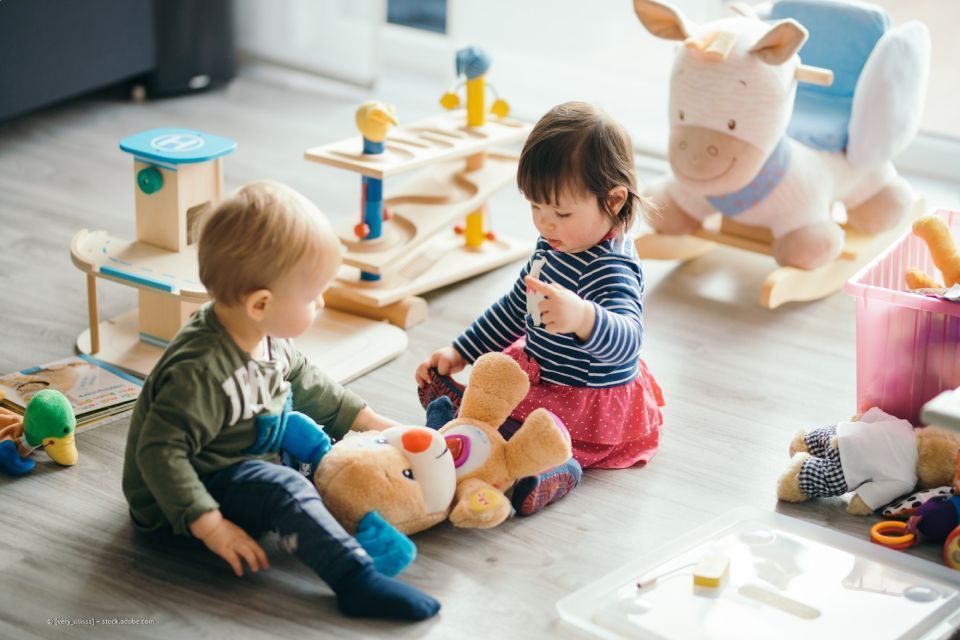 zwei Kleinkinder spielen mit einem Teddy