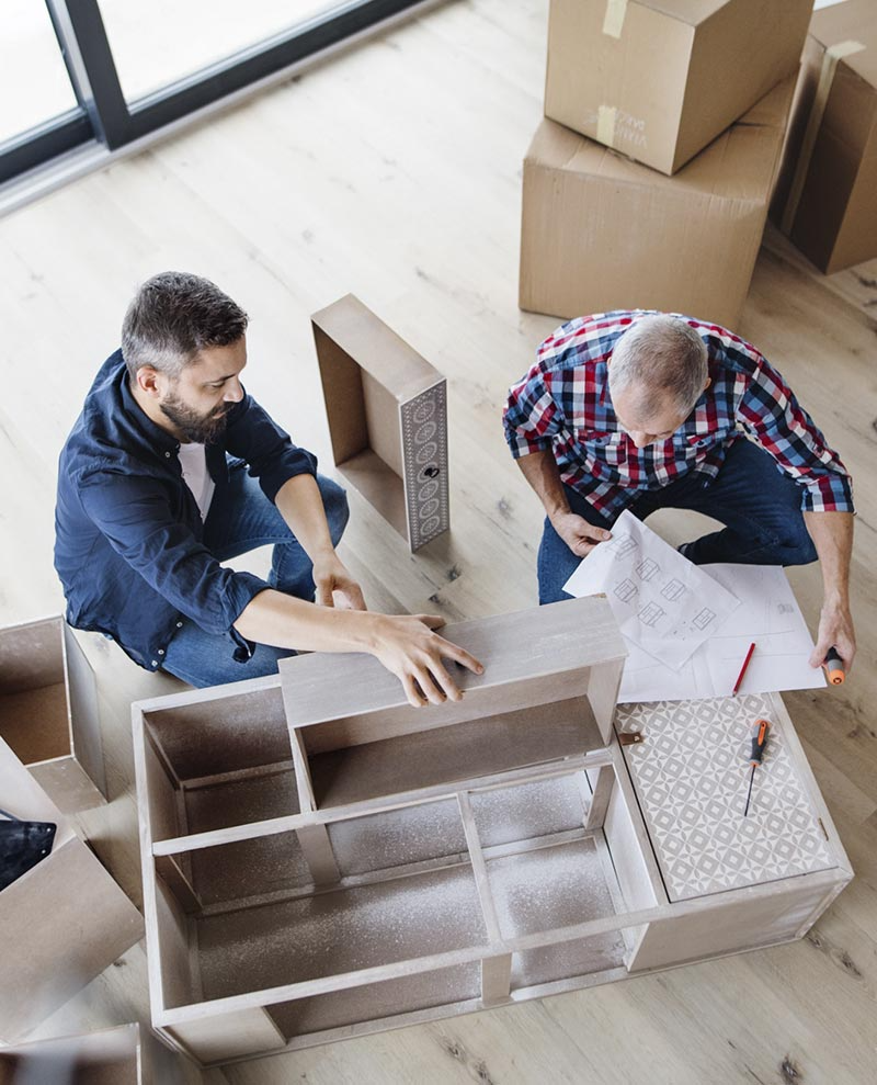 Dos hombres están sentados en una mesa trabajando en un mueble.