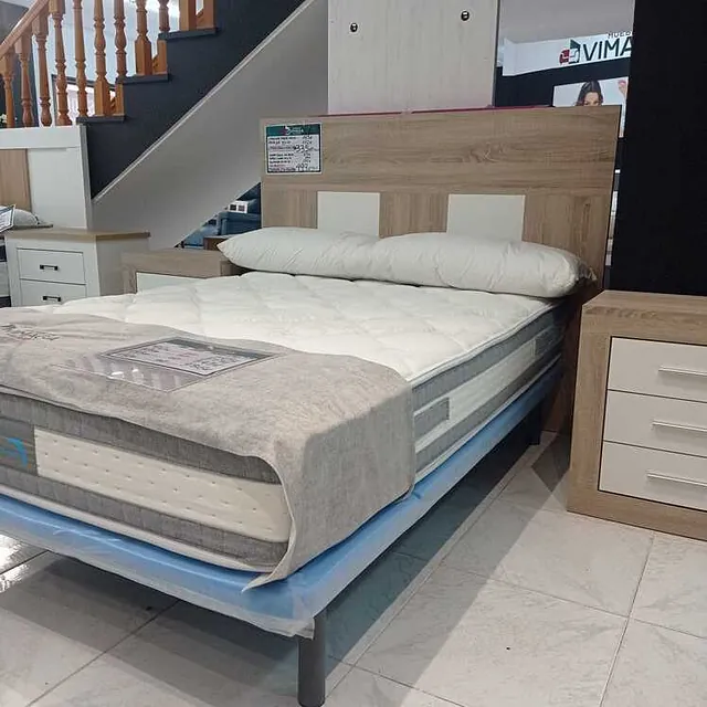 Una cama con colchón y cabecero de madera en una habitación con escaleras.