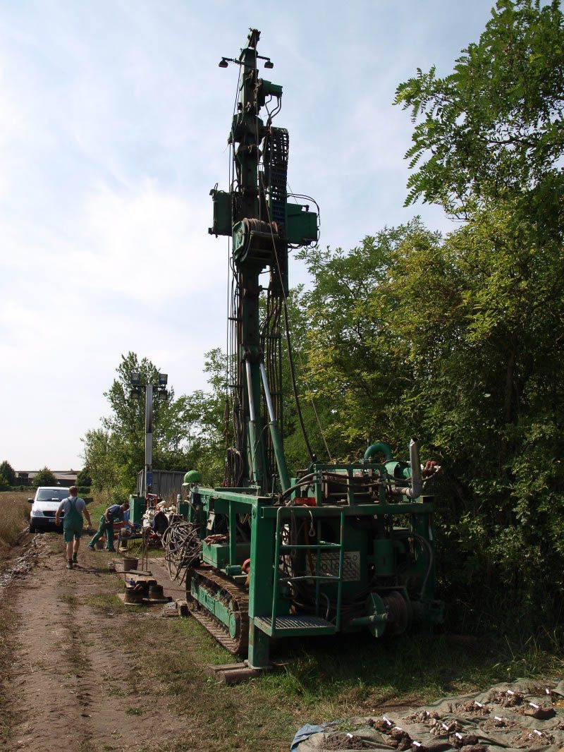 Eine große grüne Maschine steht am Rand einer unbefestigten Straße, umgeben von Bäumen - IBOTECH Bohr- und Brunnenbau GmbH aus Zöberitz bei Landsberg