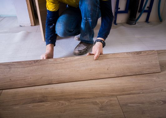Personne installant un plancher en planches marron sur un plancher bleu clair existant.
