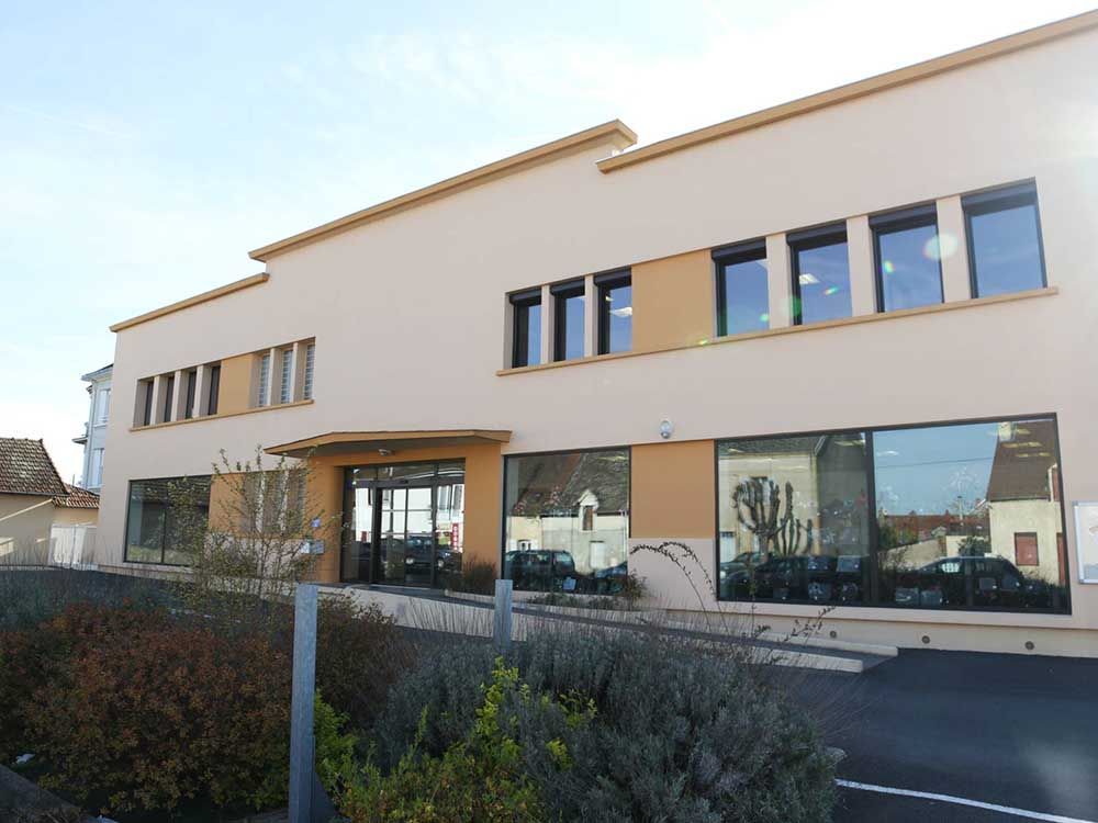 Bâtiment commercial moderne de deux étages, avec une façade beige, de grandes baies vitrées et une entrée centrale.