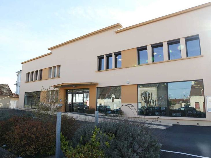 Bâtiment commercial moderne de deux étages, avec une façade beige, de grandes baies vitrées et une entrée centrale.